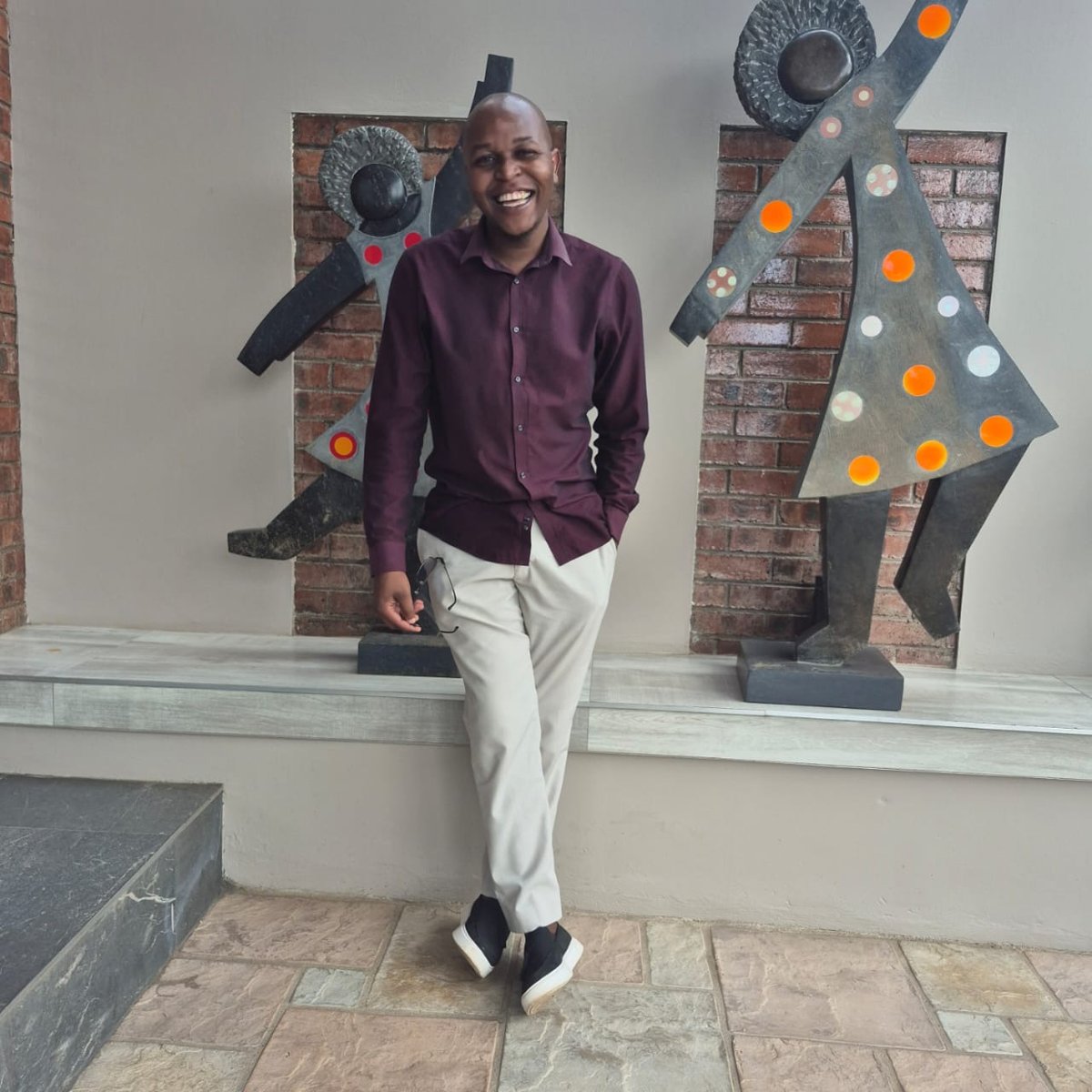 Simbarashe Able Mukondo smiling in front of sculptures in Harare